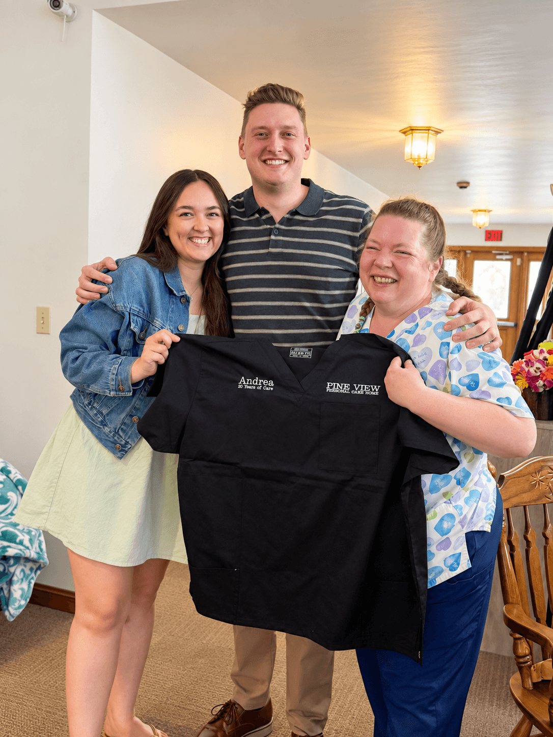 Three Pine View team members smiling together, holding up a Pine View scrub top