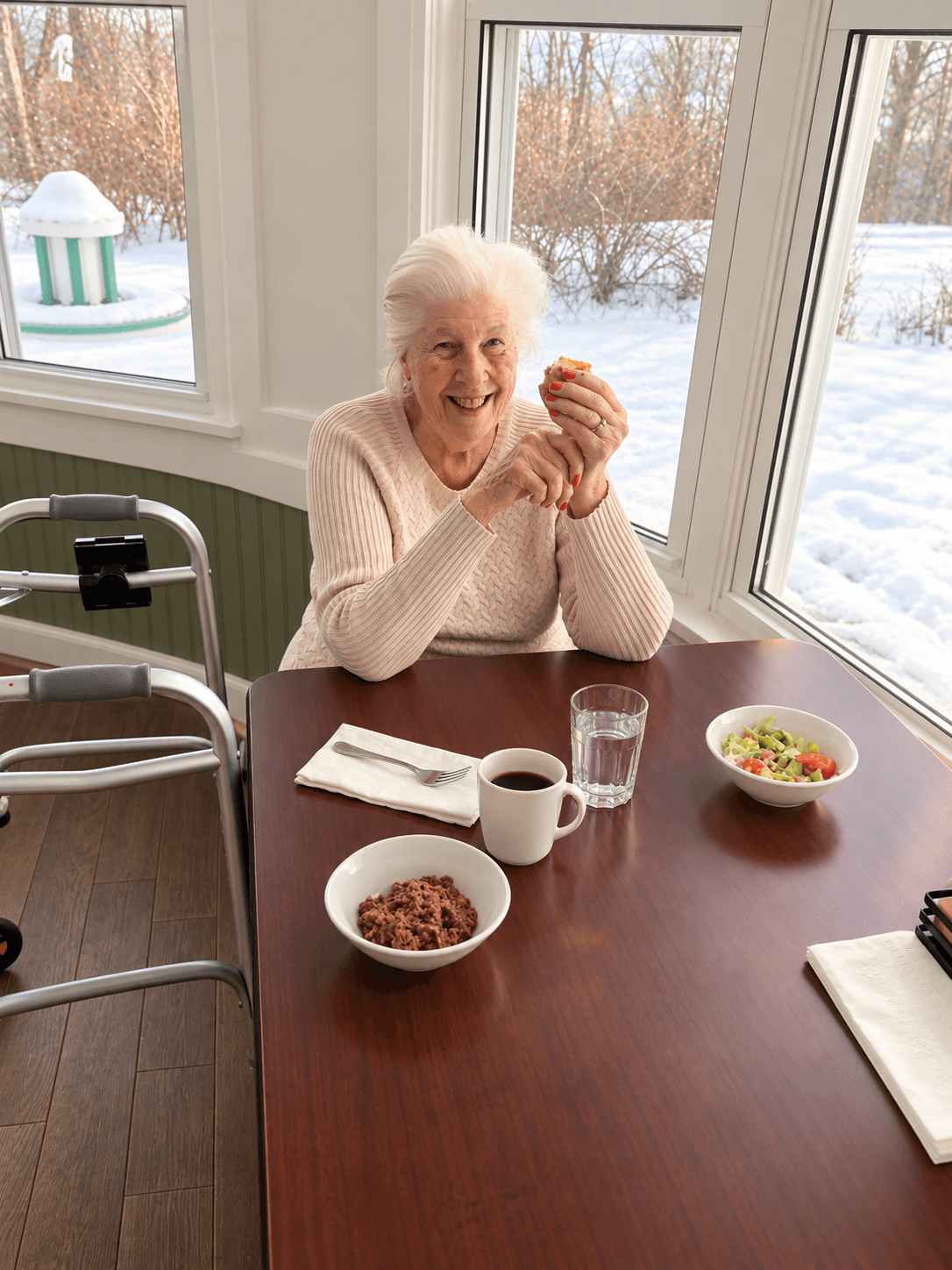 A smiling Pine View resident at the dining table by a sunny window